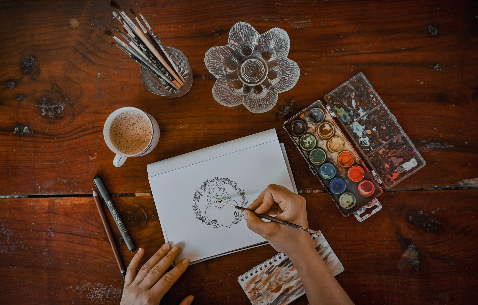Detailný záber na ruky umelca, ktorý s precíznosťou maľuje originálnu akvarelovú ilustráciu na papier. Tieto ručne maľované motívy sú následne skenované a digitálne spracované pre hrnčeky Lesovik, čím sa zaručuje ich jedinečnosť a autorský pôvod.